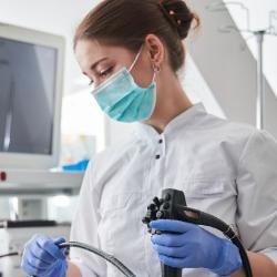 Nurse holding equipment in scrubs, gloves, and a mask.