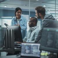 Three people huddled around a computer discussing what is on the hidden screen.