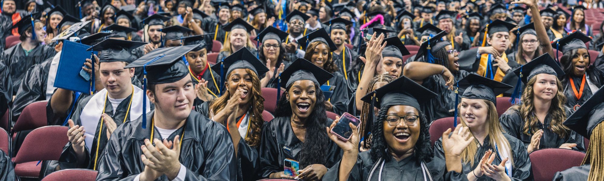 Crowd of graduates in caps and gowns cheering at commencement.